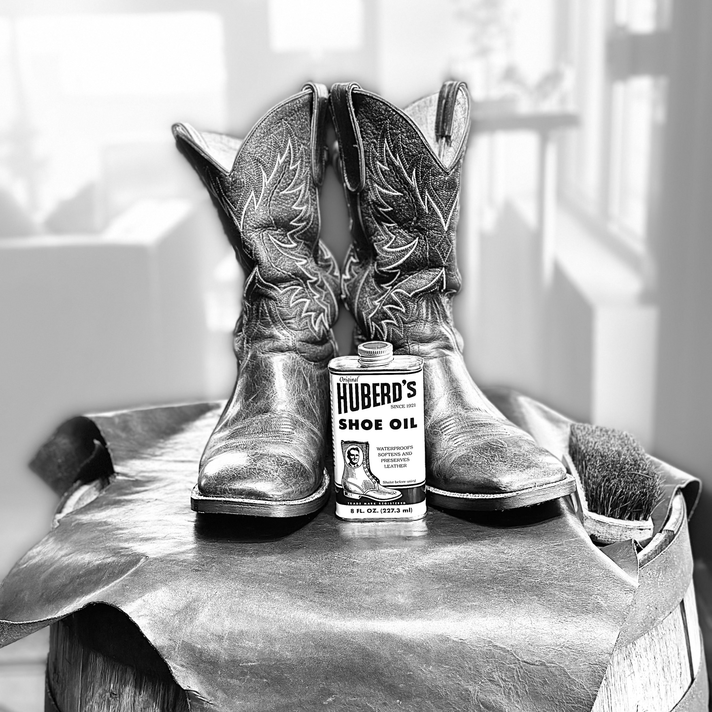 Pair of cowboy boots with a can of Hubert's Shoe Oil on a barrel